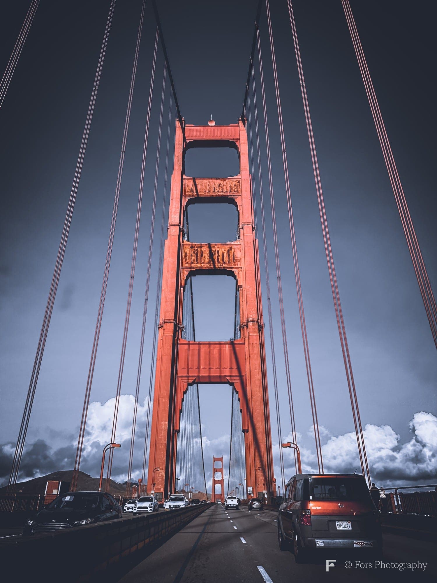 Looking up at a Golden Gate Bridge tower from the roadway, red suspender cables converging overhead and cars on the deck below.